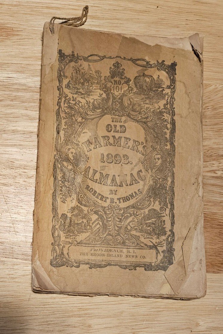 An antique farmer's almanac lying open, its aged pages printed with tables and woodcuts